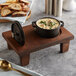 A Valor mini cast iron pot of soup on a rustic chestnut display stand.