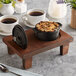 A Valor pre-seasoned mini cast iron pot on a Rustic Chestnut display stand on a table with cups of coffee and a plant.
