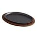 A Valor oval pre-seasoned cast iron fajita skillet on a rustic chestnut finish rubberwood platter.