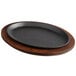 A black oval cast iron skillet on a wooden tray.