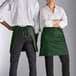A man and woman wearing Choice hunter green half bistro aprons with pockets.