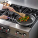 A woman using a Vollrath Wear-Ever non-stick fry pan to cook vegetables on a stove.