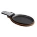 A black oval cast iron fajita skillet with a grey handle on a wood surface.