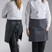 Two women in black and white striped Choice half bistro aprons on a counter in a professional kitchen.