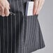 A person holding a pen in a pocket of a black and white pinstripe half bistro apron.