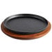 A black round pan on a wooden surface with a wooden underliner.