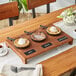 A rustic display stand holding three Valor cast iron skillets with desserts on a wood table.