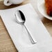 An Acopa stainless steel teaspoon on a napkin next to a croissant.