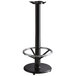 A Lancaster Table & Seating cast iron bar height table base with a metal foot rest.