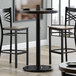 A Lancaster Table & Seating bar height table base with self-leveling feet under a table with two chairs.