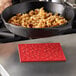 A person using a red Lodge silicone trivet to hold a black pan of food.