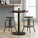 A Lancaster Table & Seating cast iron counter height table base on a table with two round wooden stools.