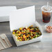 A white Fold-Pak Bio-Pak take-out box of food next to a drink and napkin with a plastic fork on the napkin.