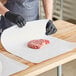 A person in black gloves using Choice white butcher paper to cut raw meat on a cutting board.