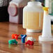 Assorted color Vollrath Traex Bar Keep II pour spouts on a table next to a bottle of liquid.