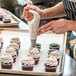 A person using a pastry bag to put Rich's Bettercreme Cookies 'N Creme Oreo whipped icing on cupcakes.