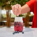 A person pouring blueberries into a jar of Rich's On Top Sweet Cream Cold Foam Topping.