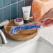 A blue twin blade disposable razor in plastic packaging placed on a wooden tray near a bathroom sink.