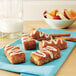 A plate of Rich's Original French Toast Sticks with white frosting and fruit on a table.