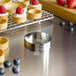 A stainless steel round tartlet ring with a pastry in it on a metal tray with fruit.
