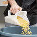A hand using a Rubbermaid Bouncer utility scoop to pour pasta into a container.