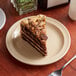 A slice of chocolate cake on an Acopa tan narrow rim melamine plate next to a fork.