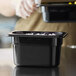 A person holding a black Vigor polycarbonate food pan filled with food on a counter.