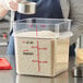 A woman pouring a measuring cup of white rice into a Vigor food storage container on a kitchen counter.