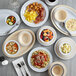 A table with Acopa Foundations tan narrow rim melamine plates and bowls of food and utensils.