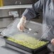 A person wearing gloves uses a Vigor clear polycarbonate food pan lid to cover food.