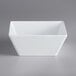 An Acopa Rittenhouse white square melamine bowl on a gray surface.