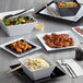 A table set with Acopa Rittenhouse black square melamine plates filled with a variety of food