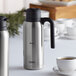 A silver and black Thermos stainless steel carafe on a table.