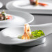 A Corona by GET Enterprises bright white porcelain plate with shrimp and a garnish on it.