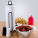 A black metal Choice paper towel holder on a counter next to a bowl of chicken and french fries.