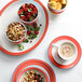 A stackable coral porcelain bowl filled with mixed nuts and berries on a plate with a cup of coffee.