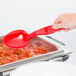 A hand using a Cambro red plastic salad bar spoon to serve food.