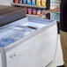 A person opening an Avantco glass top display freezer.