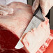 A person using a Mercer European Butcher Knife to cut meat on a counter.