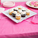 A white square melamine plate with cupcakes topped with white frosting and sprinkles on it.