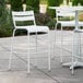 A Lancaster Table & Seating white powder coated aluminum outdoor bar stool on a patio with a white table and chairs.