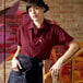 A woman leaning on a wooden handrail wearing a burgundy Uncommon Chef cook shirt.