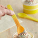 A hand holding a yellow spoon over a cup of frozen yogurt.