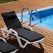Two black Lancaster Table & Seating chaise loungers with cushions and pillows next to a pool.