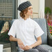 A woman wearing a white Uncommon Chef cook shirt with a black striped hat sitting in a chair.