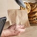 A hand placing a stack of cookies in a natural kraft paper bag.