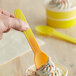 A hand holding a yellow spoon over a cup of ice cream.