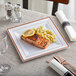 A Visions white plastic plate with rose gold bands holding food with a lemon wedge on top.