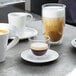 A Villeroy & Boch double wall glass cup with brown liquid and white foam next to a glass of brown liquid.