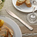 A Visions rose gold plastic knife on a plate with food and a glass of wine.